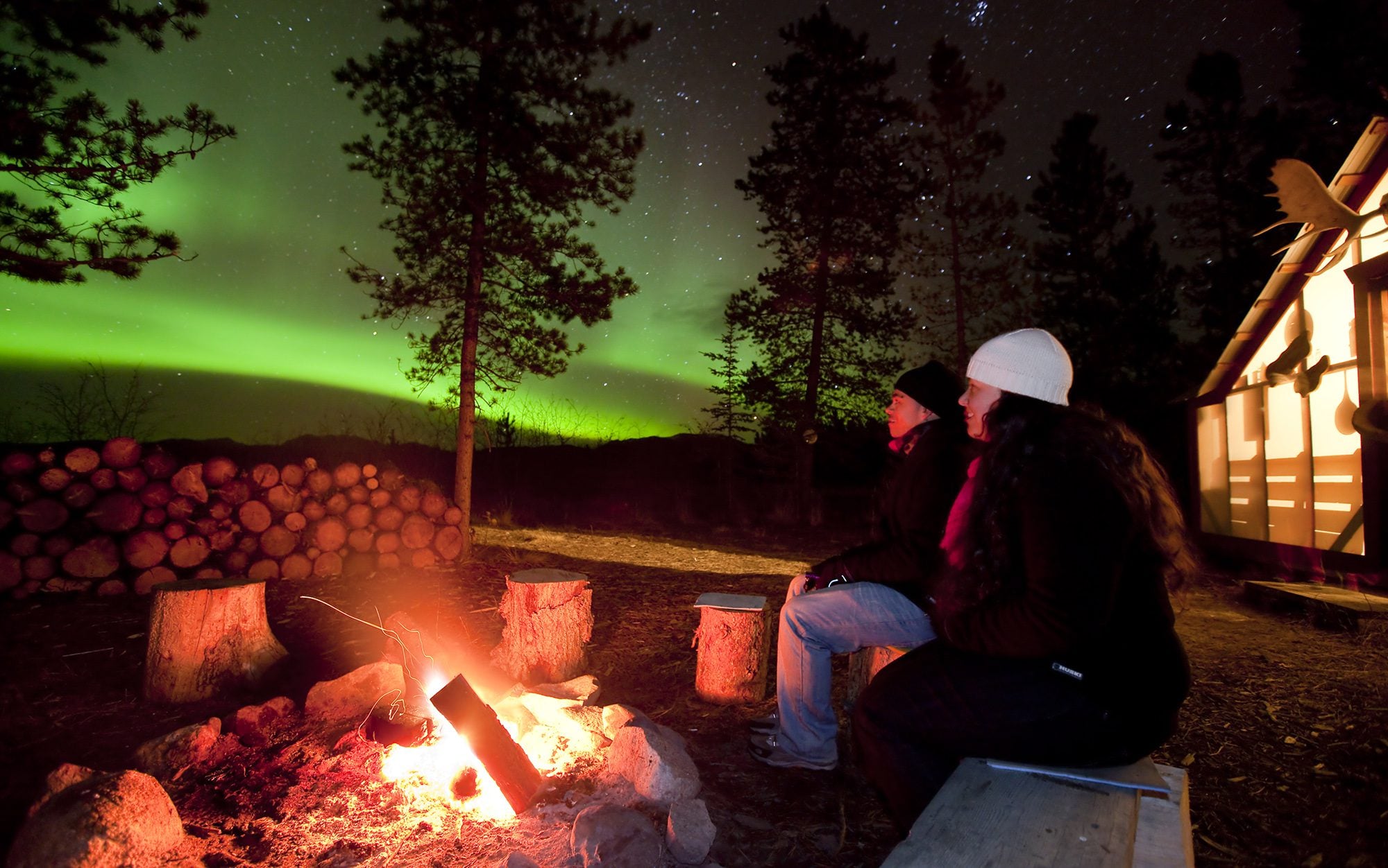 woman at a campfire watching the northern lights in the Yukon with mosaic earth travel based in canada