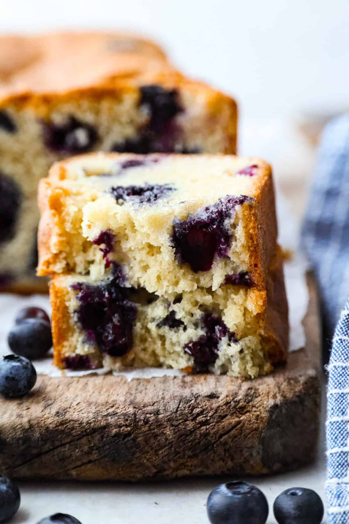 This 5 Ingredient Blueberry Bread is the little shortcut loaf you’ll make once and then suddenly need every weekend. It’s soft, sweet, full of juicy blueberries, and comes together with only five simple ingredients. Close up shot of a slice of a 5 ingredient blueberry bread slice cut in hlaf ans stacked.