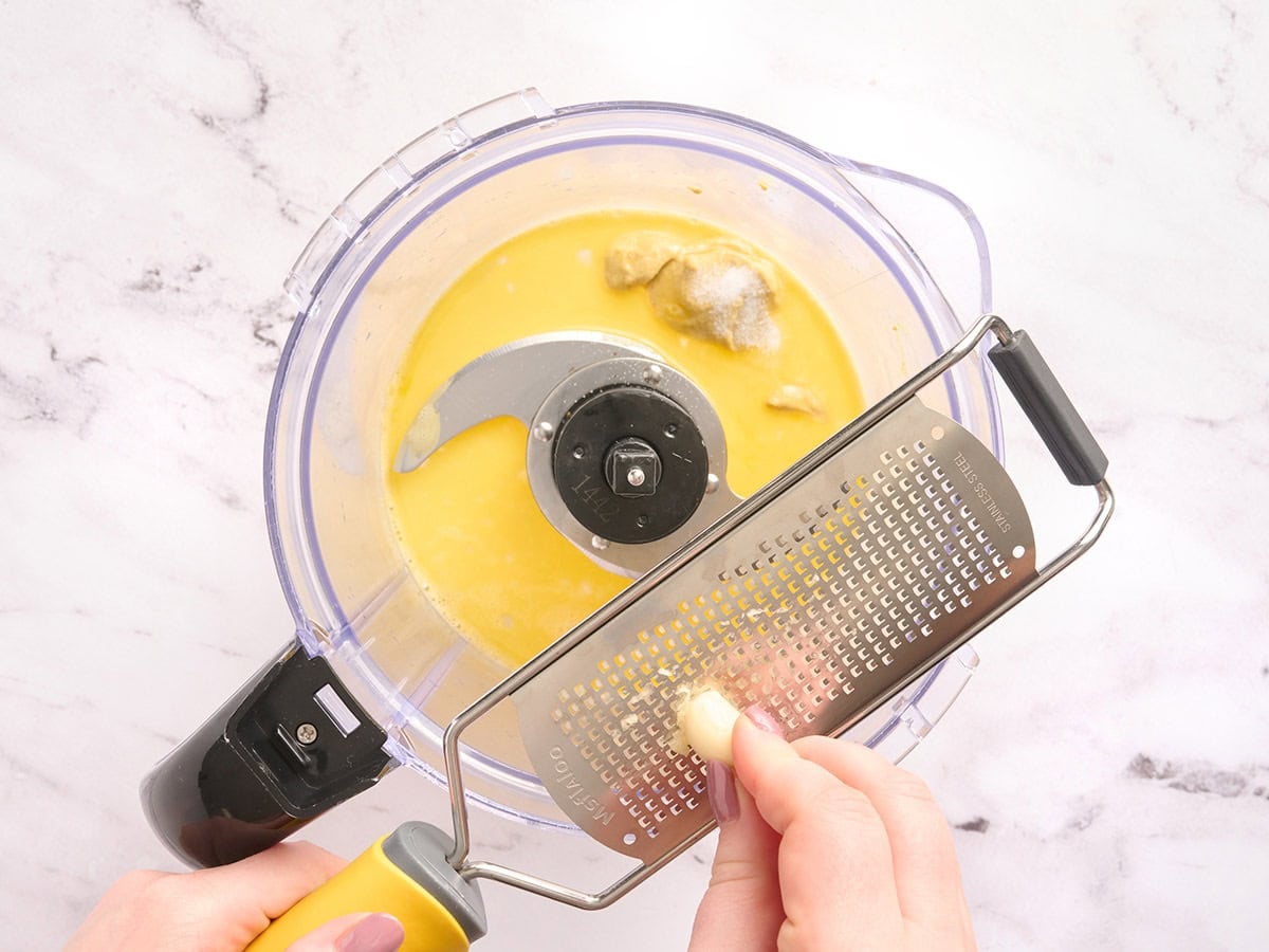 Hands grating a garlic glove into a food processor.