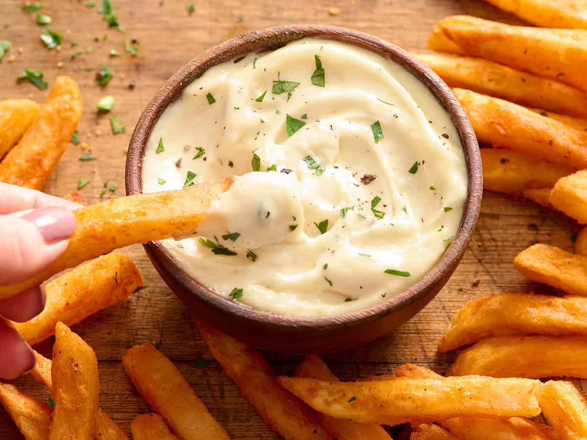 Overhead side view of a bowl of homemade garlic aioli with a French fry being dipped into it.