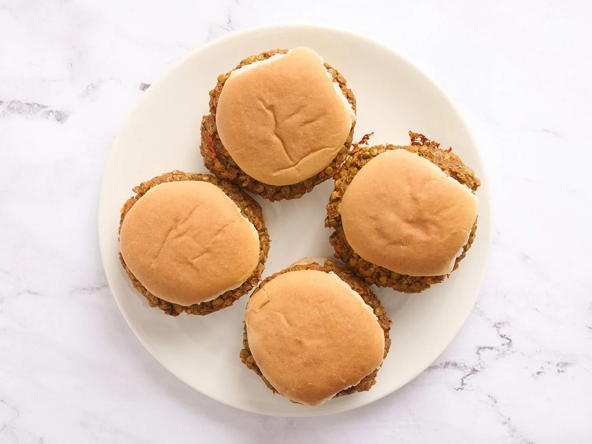 Overhead view of four lentil burgers in hamburger buns on a plate.