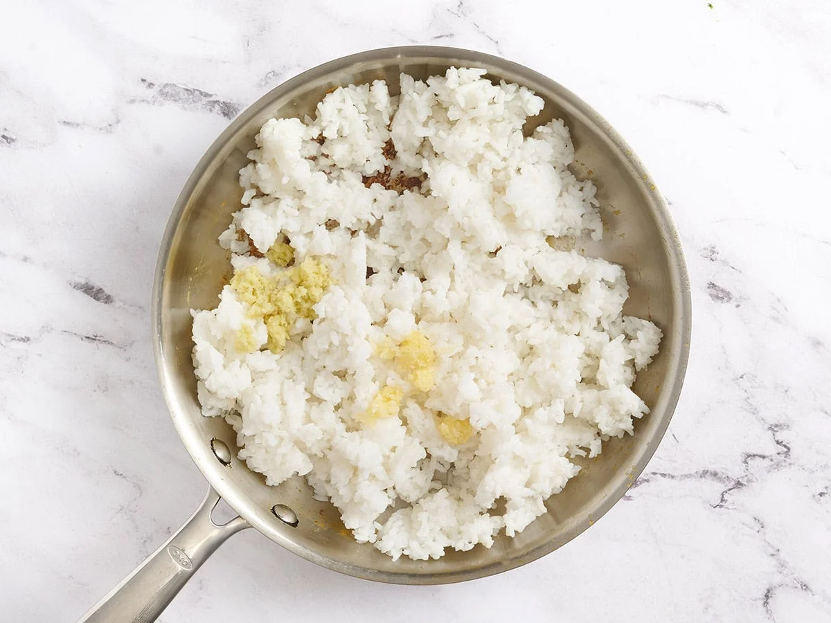 Ginger and garlic added to a skillet with rice.