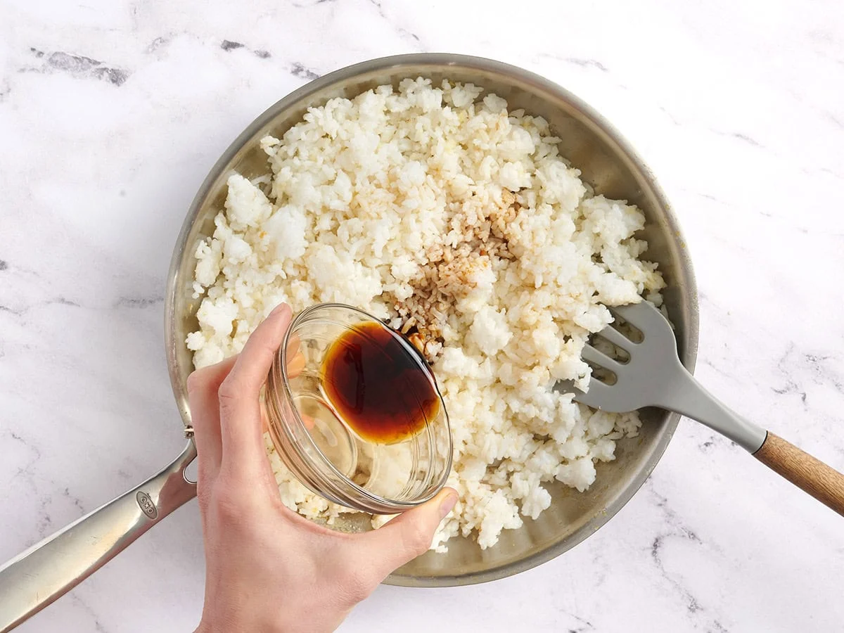 Sesame oil and soy sauce added to a skillet of rice.