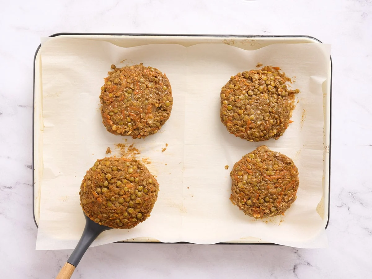 Lentil burgers on a sheet pan being flipped over halfway through cooking with a spatula.