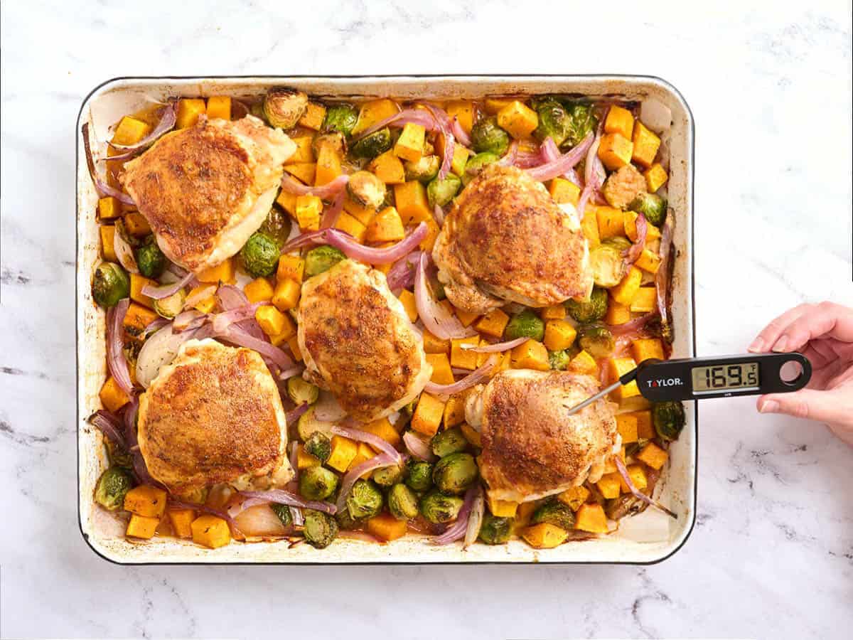 A thermometer checking the internal temperature of baked chicken thighs.