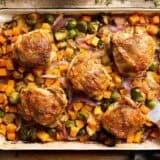 Overhead view of sheet pan chicken thighs with a metal spatula taking some.