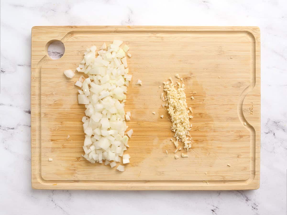 Diced onion on a wooden cutting board with minced garlic.