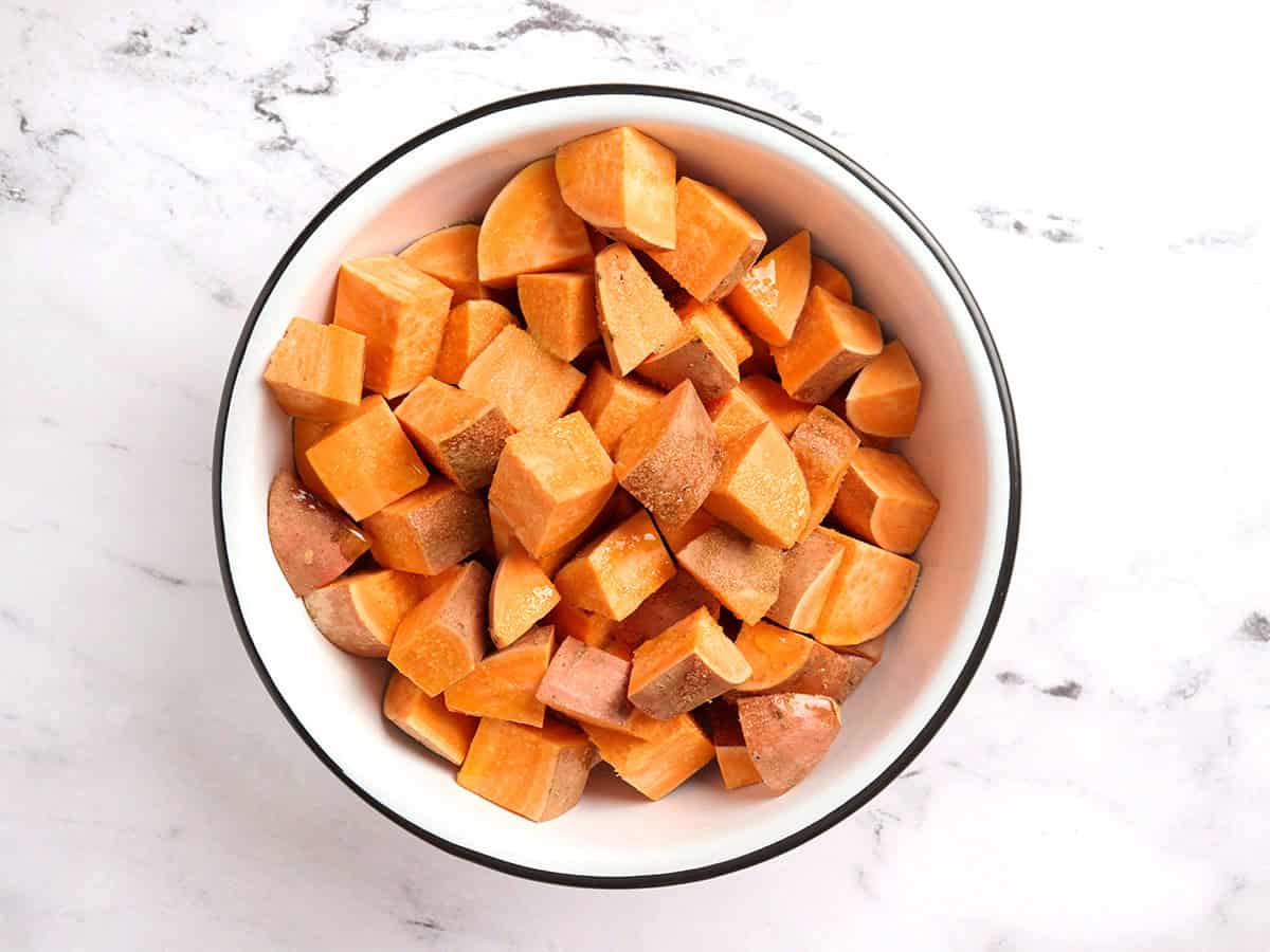 Diced sweet potatoes in a bowl with oil and salt.