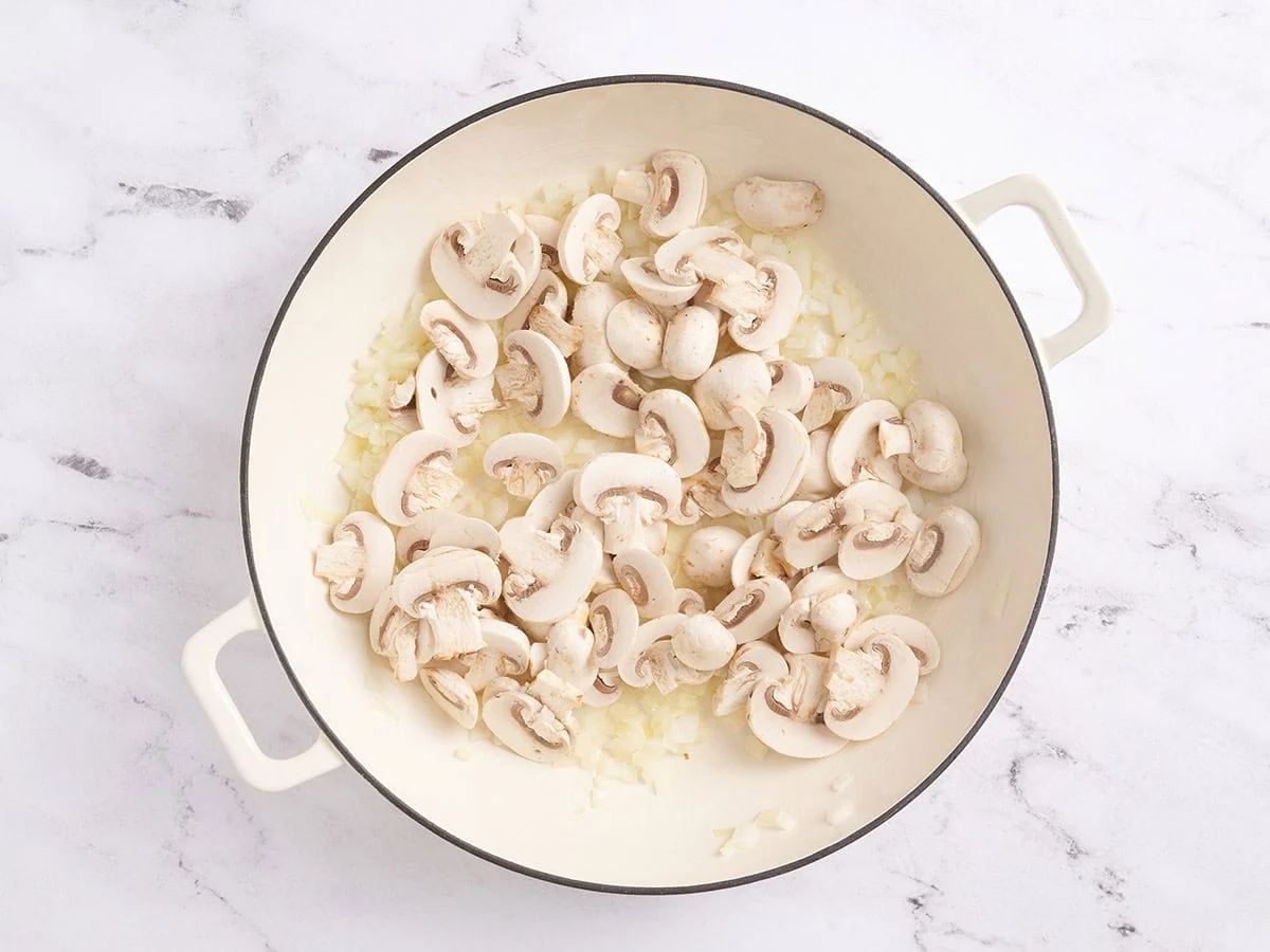 Mushrooms added to a skillet with sauteed onions.