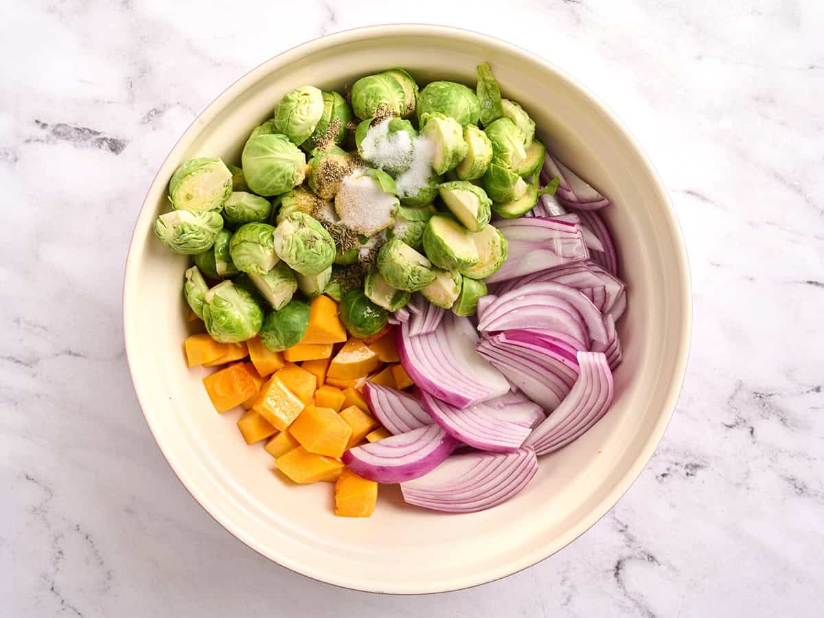 Chopped brussels sprouts, red onion and butternut squash in a mixing bowl.