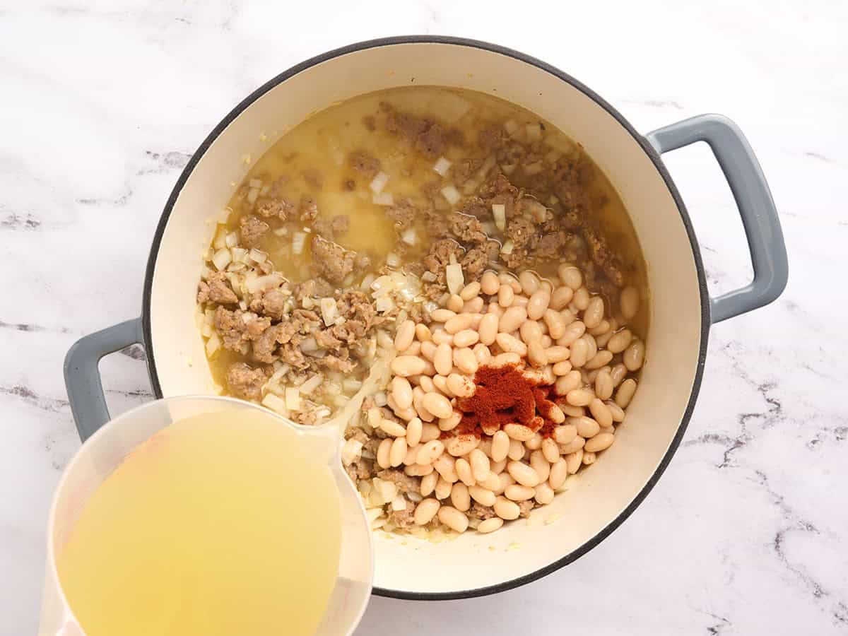 Broth being poured into a pot of beans and seasoning.
