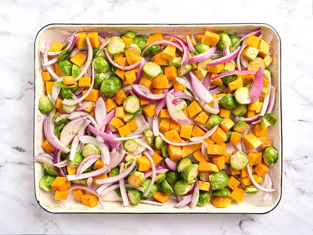 Chopped red onion, butternut squash and brussels sprouts on a sheet pan.