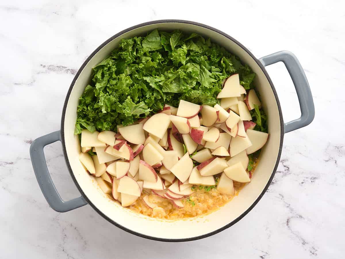 Kale and potatoes added to a pot of soup.