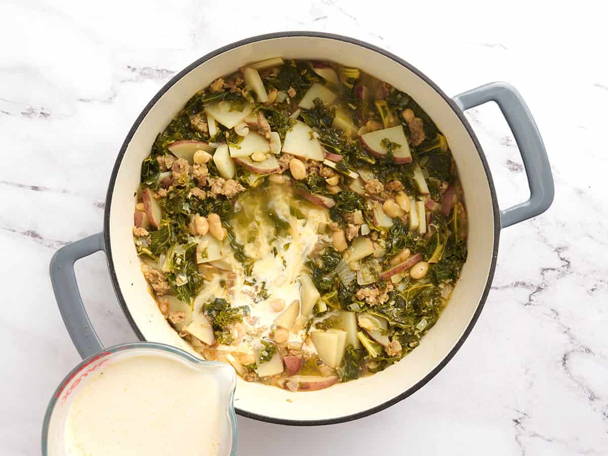Half and half being poured into a pot of homemade zuppa toscana.