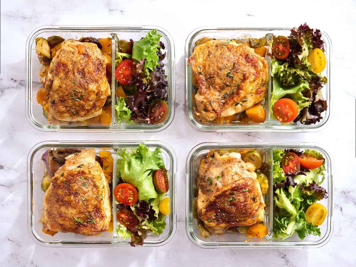 Overhead view of meal prepped sheet pan chicken thighs in meal prep containers.