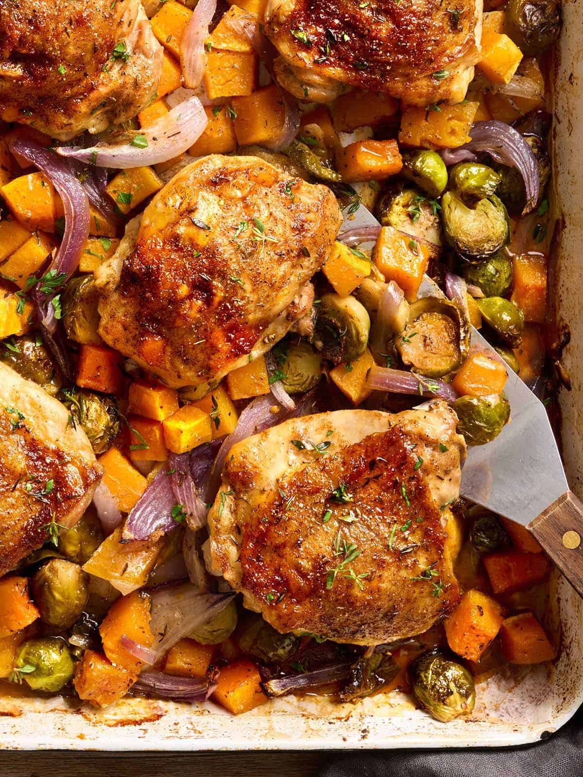 Overhead view of sheet pan chicken thighs with a metal spatula taking some.