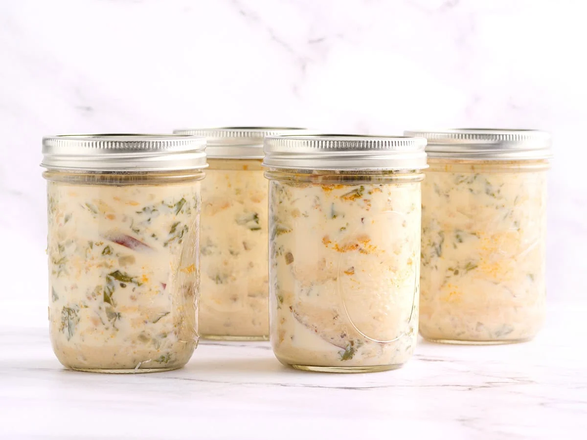 Side view of zuppa toscana soup in mason jars with glass lids.