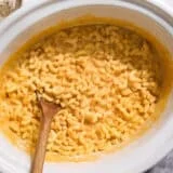Overhead view of creamy crockpot mac and cheese in a slow cooker with a wooden spoon.