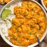 Overhead view of a bowl of pumpkin curry with white rice and a lime wedge.