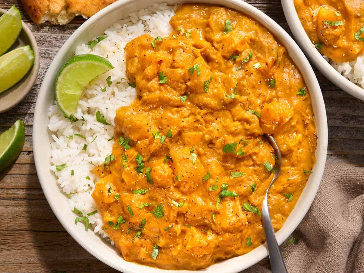 Overhead view of a bowl of pumpkin curry with white rice and a lime wedge.