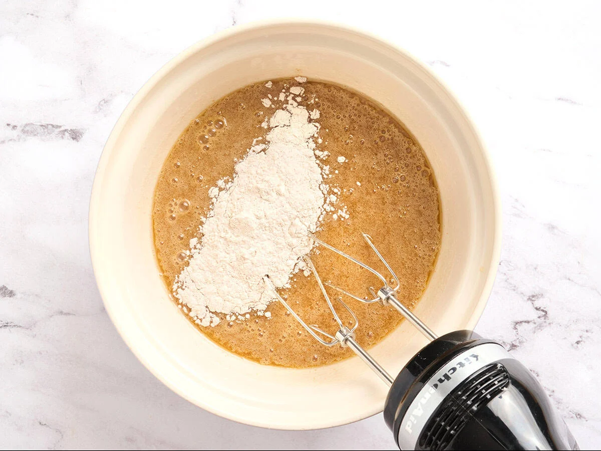 Dry ingredients being added to the wet batter in a mixing bowl.