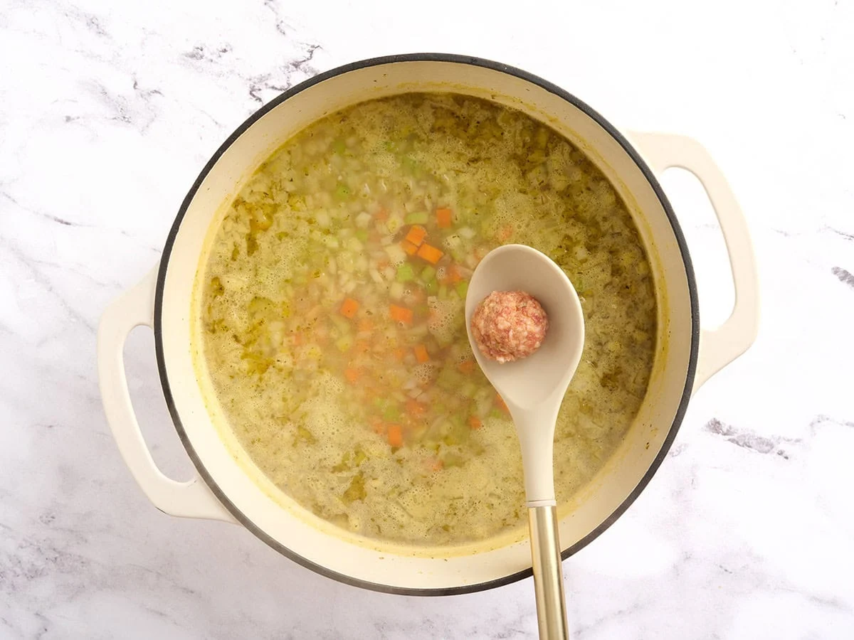 A raw meatball being added directly to a pot of soup.