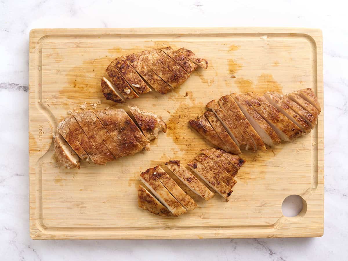 Sliced jerk chicken on a wooden cutting board.