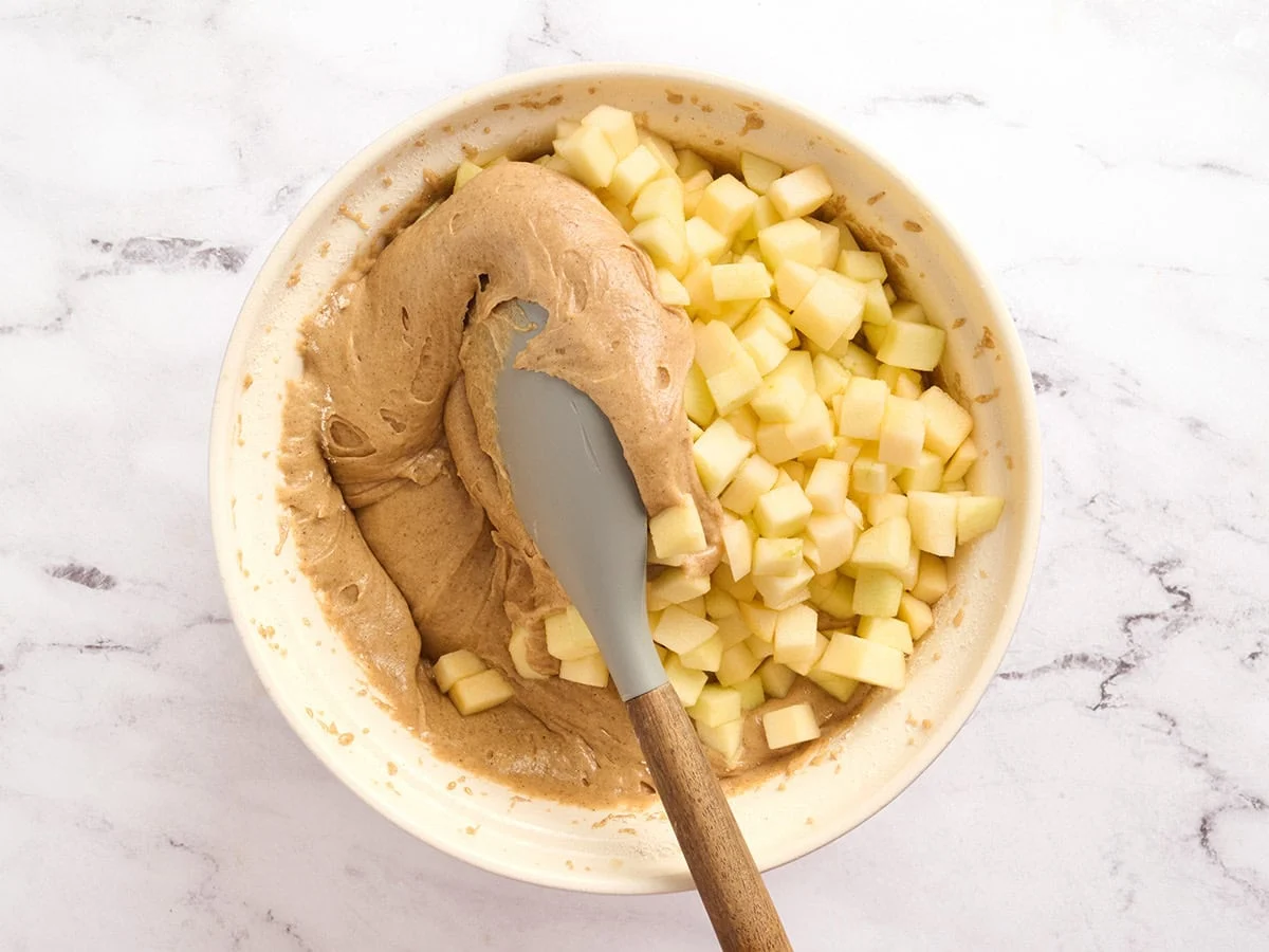 Diced apples being folded into the batter for an apple spice cake.