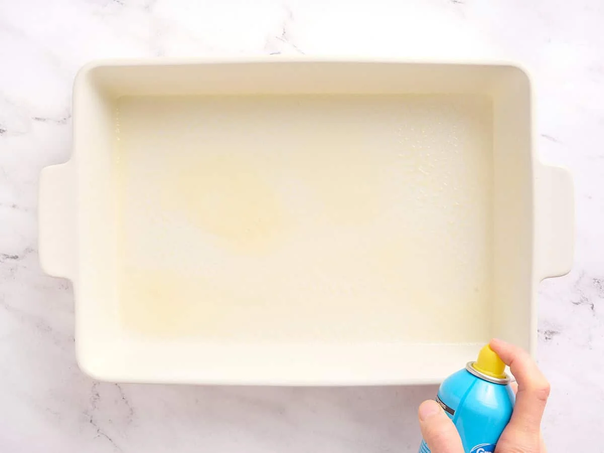A baking dish being sprayed with non stick spray.