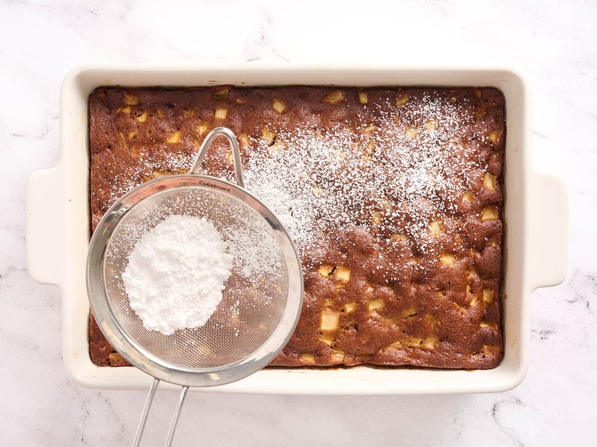 An apple spice cake being sprinkled with powdered sugar.