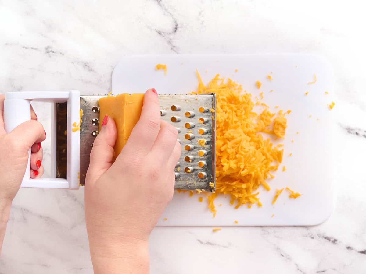 Hands using a cheese grater to shred cheese.