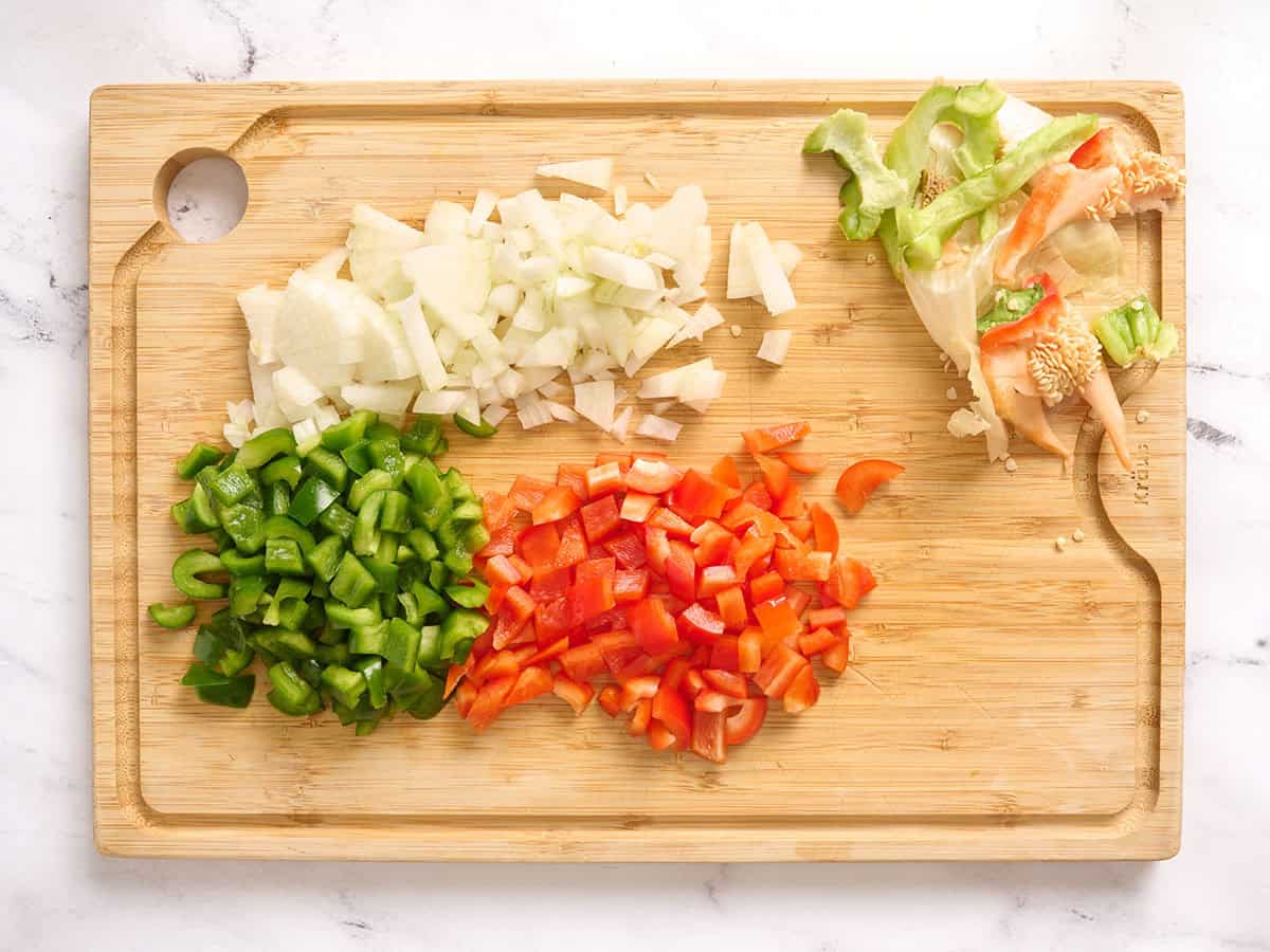 Diced onion, green bell pepper and red bell pepper on a wooden cutting board.