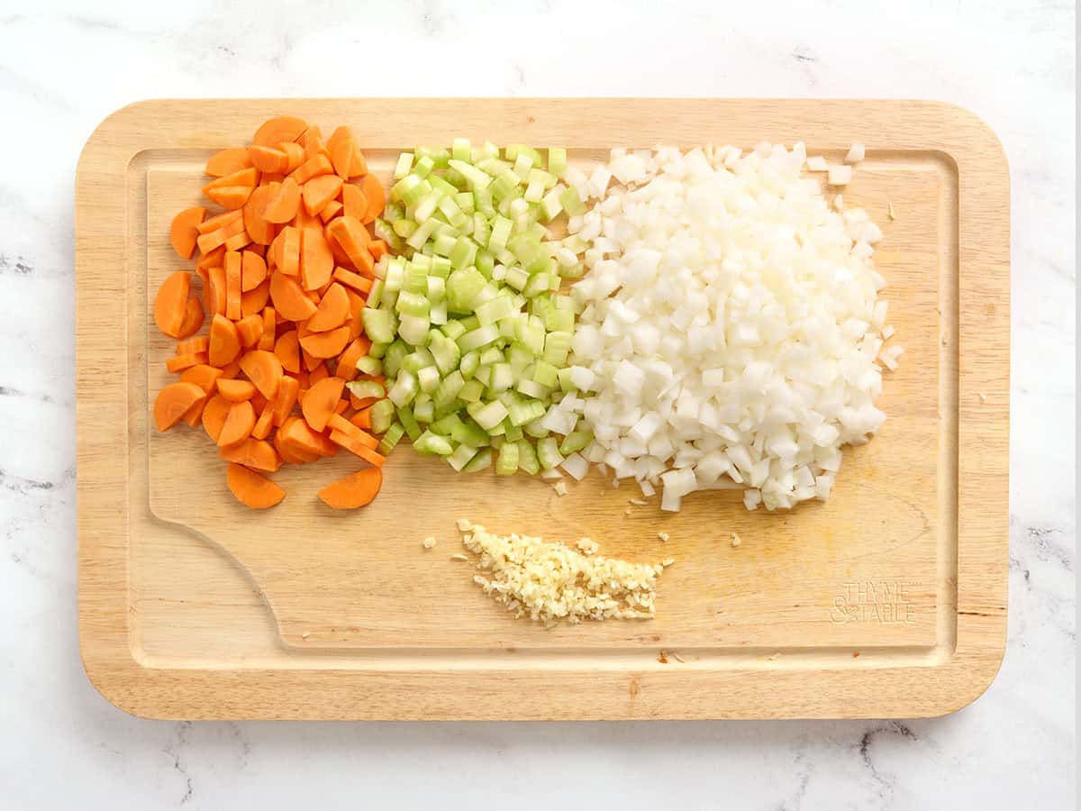 Diced carrots, onions and celery on a wooden cutting board with minced garlic.