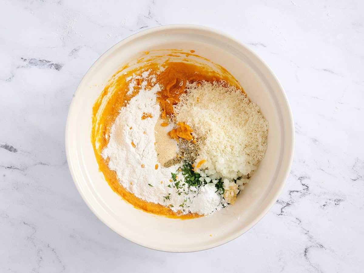 Flour, seasonings, and parmesan cheese added to pumpkin in a mixing bowl.