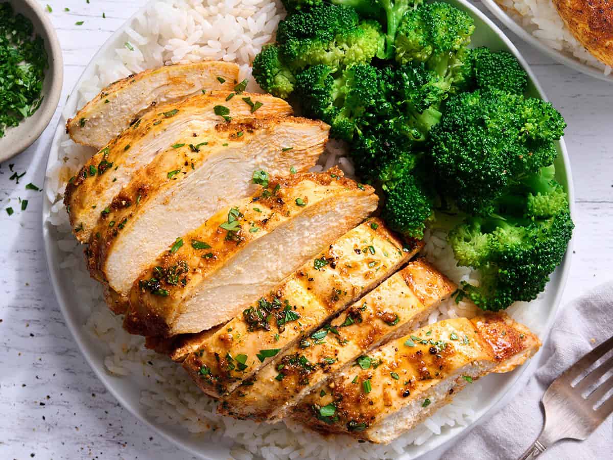 Overhead view of sliced baked chicken breast on a bed of rice with broccoli.