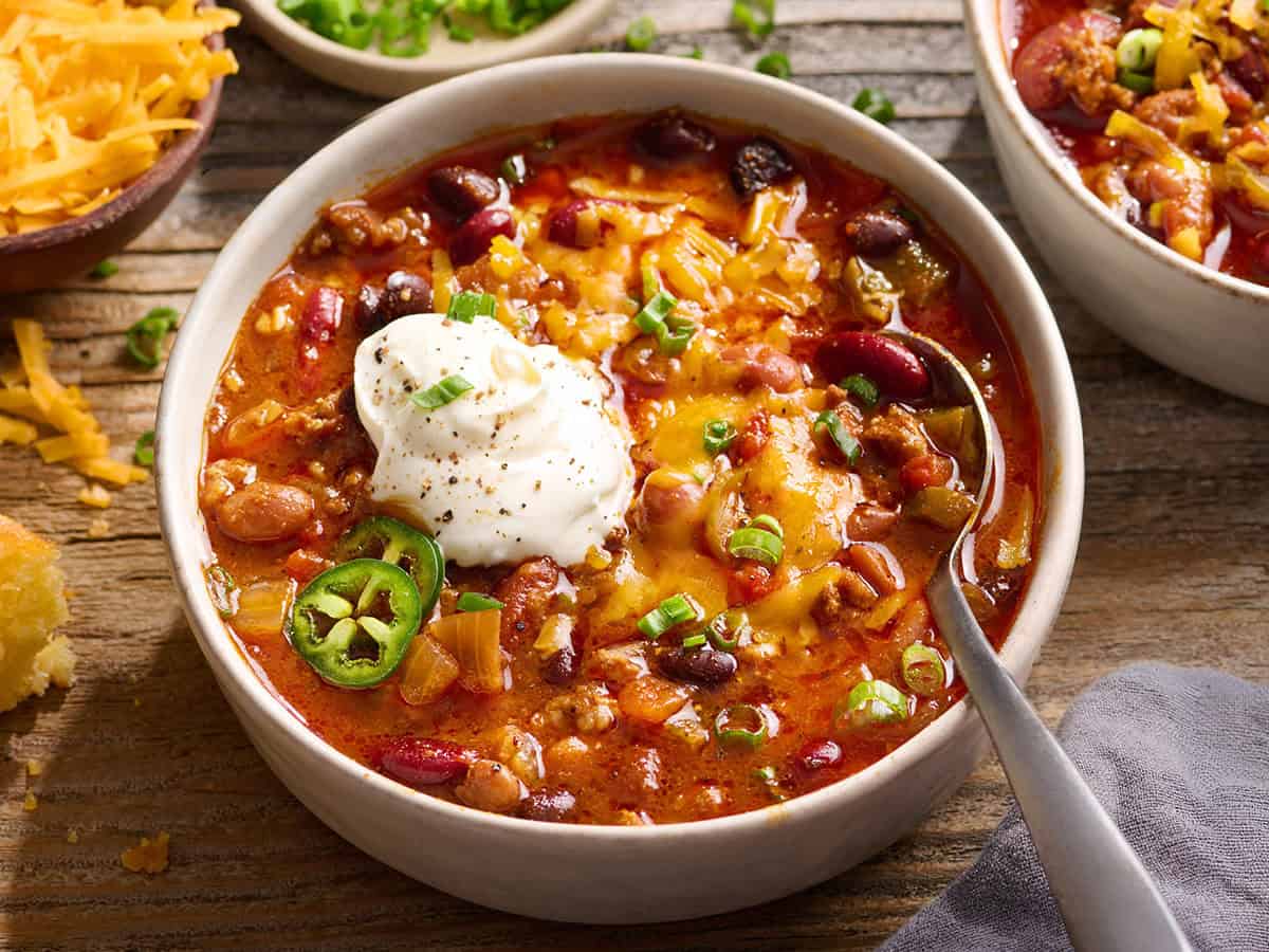Side front view of a bowl of crockpot chili with sour cream and shredded cheese.