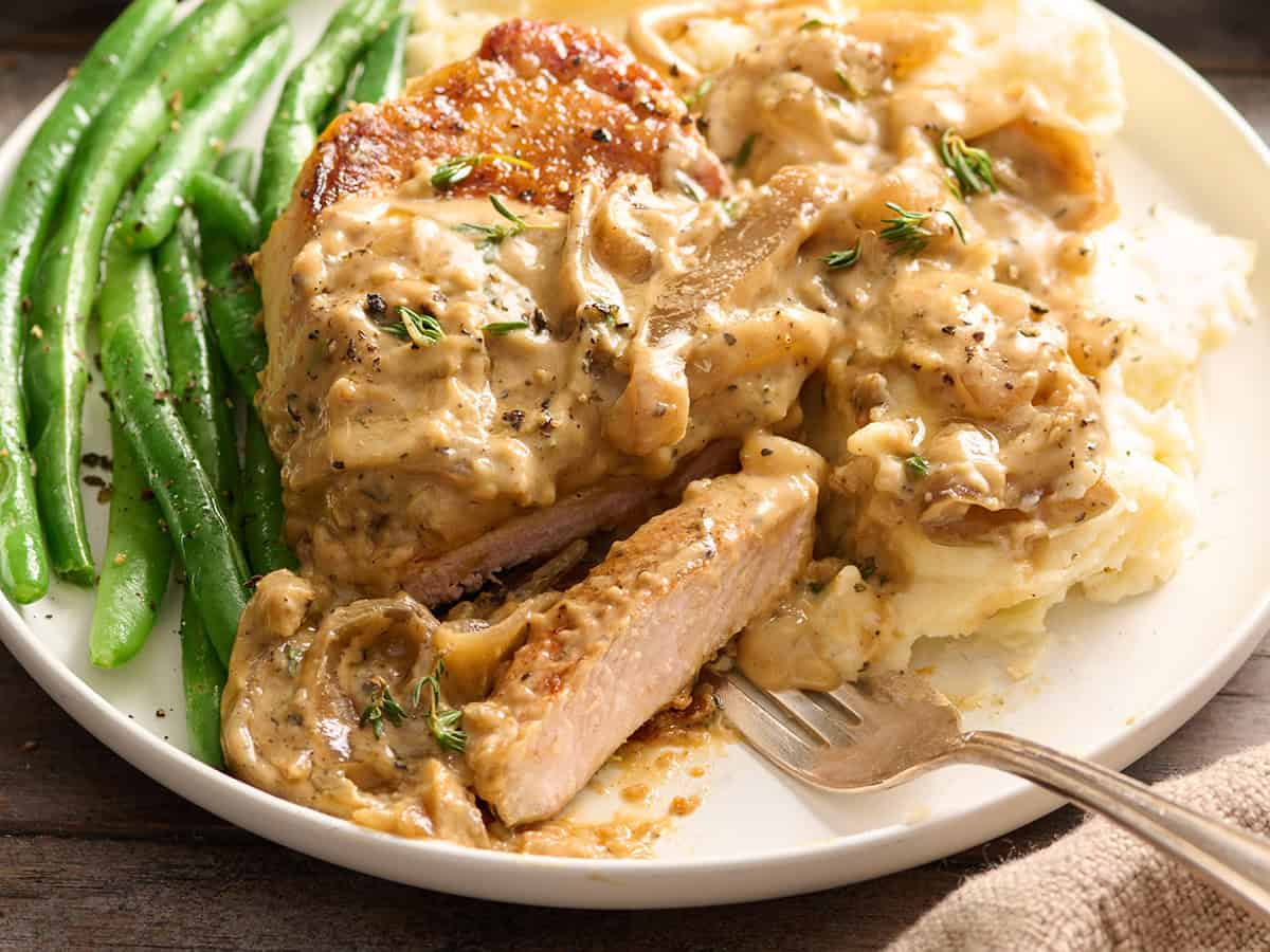 Side view of smothered pork chops on a plate with a fork and green beans.