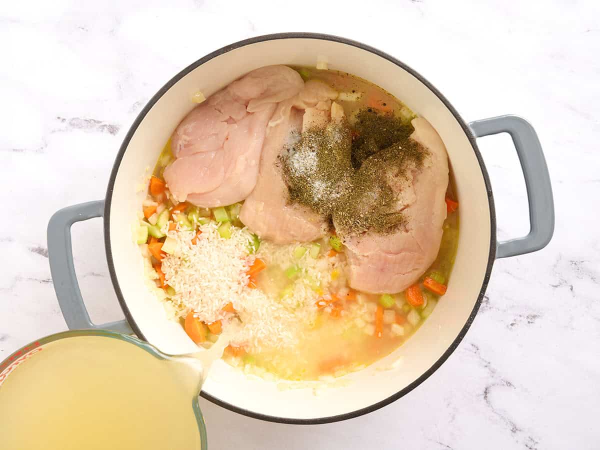 Raw chicken and seasonings added to a pot with sauteed veggies and broth.