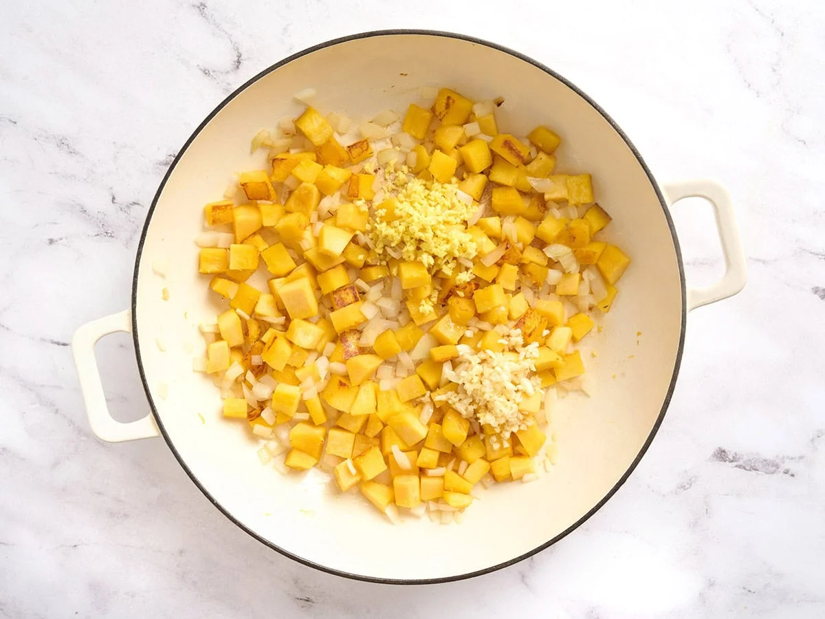 Garlic and ginger added to diced pumpkin in a pot.