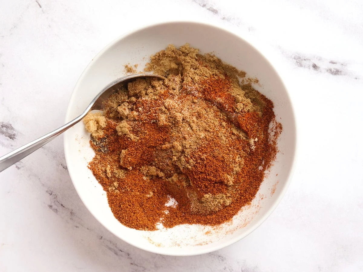 A spoon mixing a homemade chili seasoning in a bowl.