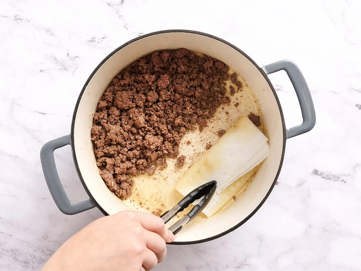Kitchen tongs using a paper towel to soak grease from ground beef.
