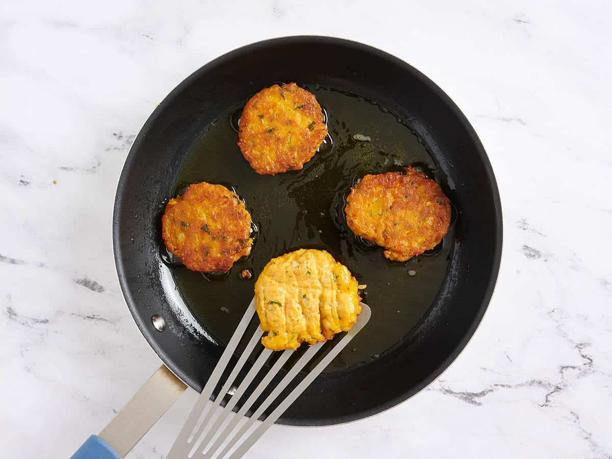 A spatula flipping a pumpkin fritter cooking in a skillet.