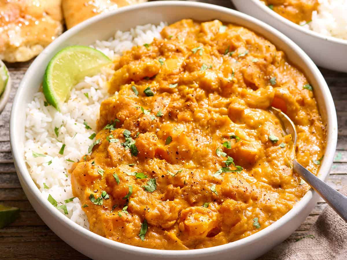Side view of a bowl of pumpkin curry with white rice.
