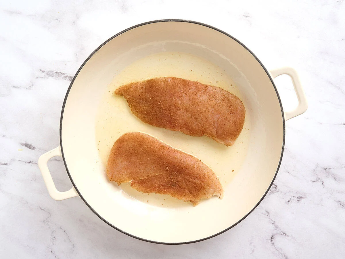 Seasoned chicken breast cooking in a skillet.