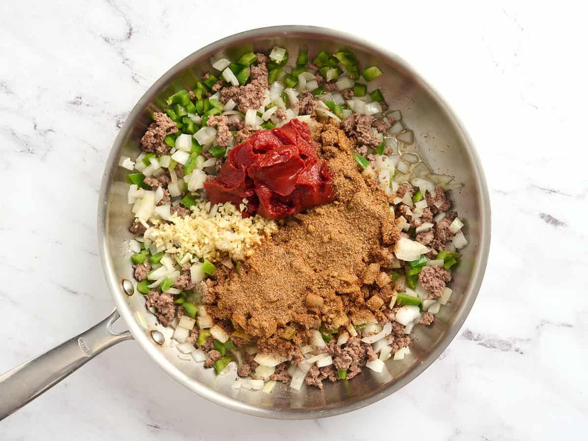 Diced bell pepper, garlic and onion added to a skillet with browned ground beef and seasoning.