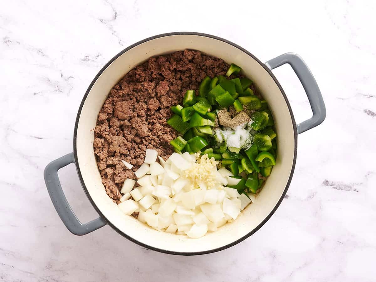 Diced onion and pepper peppers added to browned ground beef in a pot.