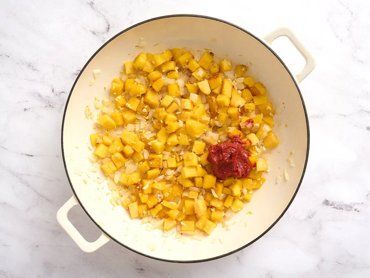 Tomato paste added to a pot with diced pumpkin.
