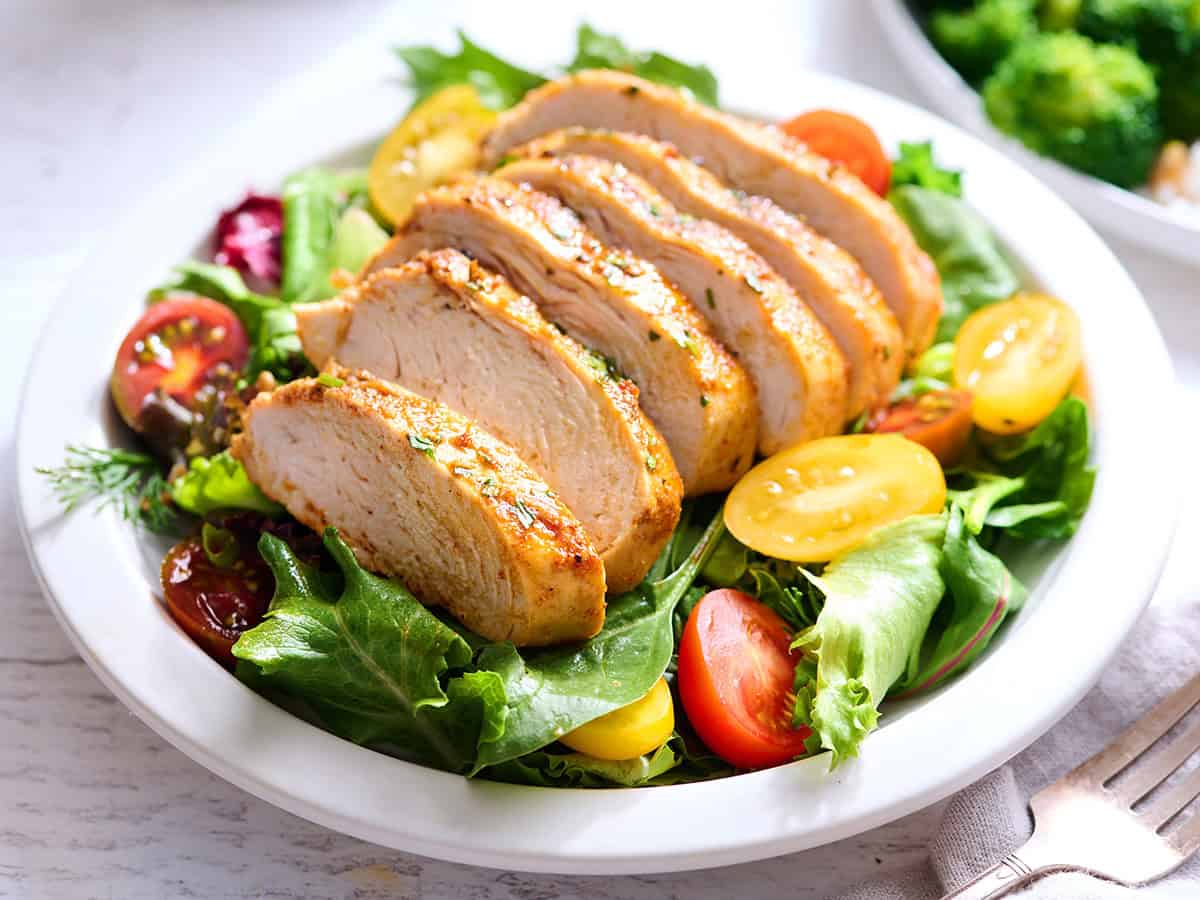 Side view of sliced chicken breast on a bed of salad in a bowl.