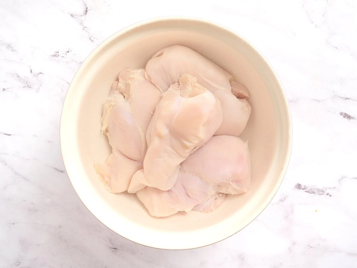 Overhead view of chicken breasts in a brine in a mixing bowl.