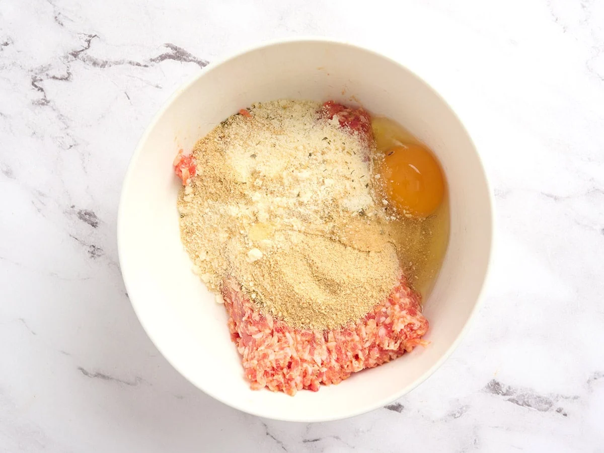 Egg, breadcrumbs, parmesan and ground meat in a bowl.